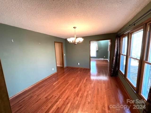 unfurnished room with hardwood / wood-style floors, a textured ceiling, and an inviting chandelier