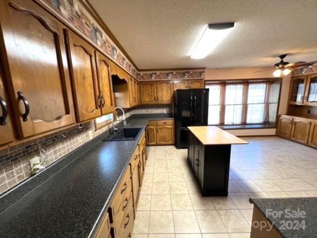 kitchen with black refrigerator, backsplash, ceiling fan, sink, and a center island