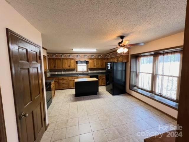 kitchen featuring black fridge, ceiling fan, sink, a kitchen island, and light tile patterned flooring