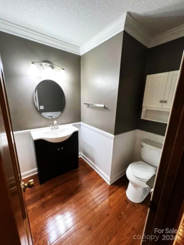 bathroom featuring hardwood / wood-style floors, vanity, toilet, ornamental molding, and a textured ceiling