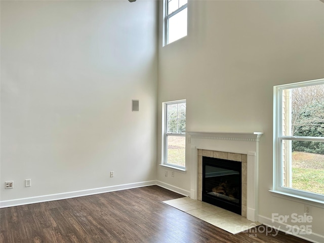 unfurnished living room featuring light hardwood / wood-style flooring, a towering ceiling, a wealth of natural light, and a tile fireplace