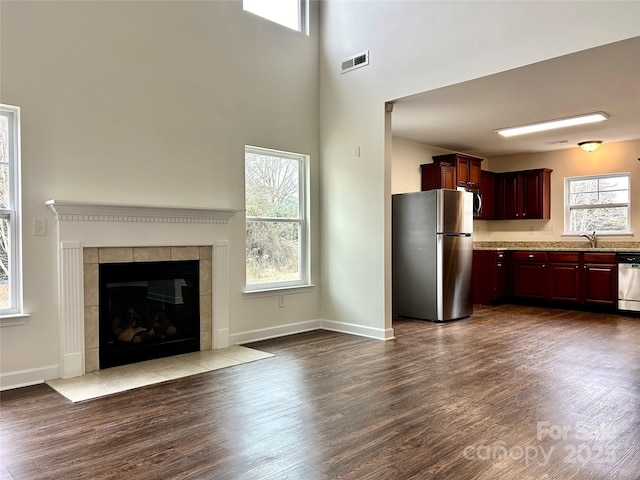 unfurnished living room with a fireplace, dark wood-type flooring, sink, and a towering ceiling