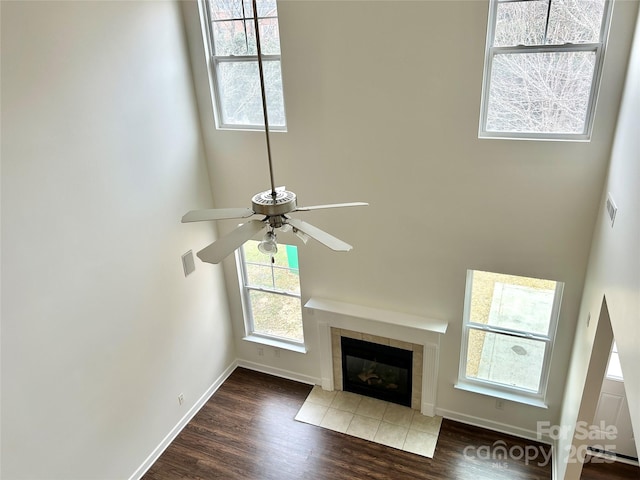 unfurnished living room with a towering ceiling, dark wood-type flooring, ceiling fan, and a tiled fireplace