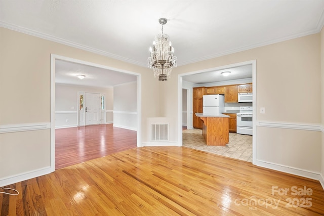 interior space featuring an inviting chandelier, ornamental molding, and light hardwood / wood-style floors