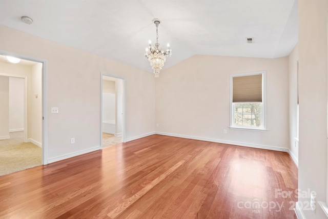 spare room featuring hardwood / wood-style floors, vaulted ceiling, and a chandelier