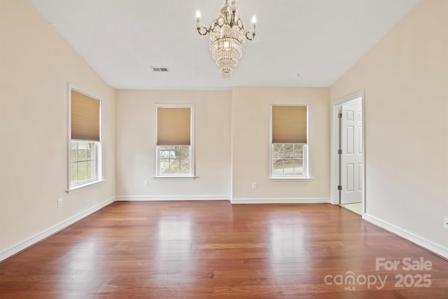 empty room featuring wood-type flooring and a notable chandelier