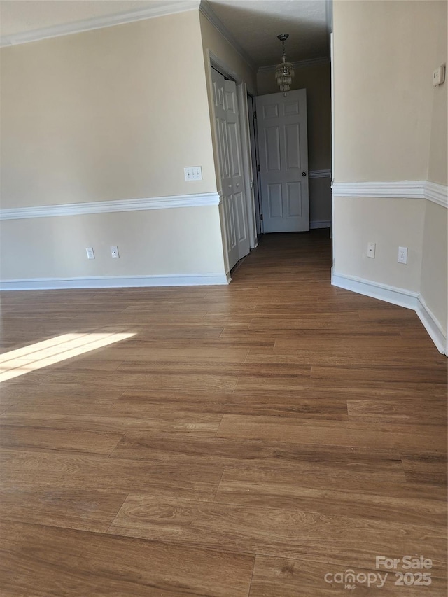 empty room with ornamental molding, wood-type flooring, and a chandelier