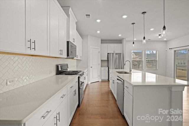 kitchen with a kitchen island with sink, decorative backsplash, appliances with stainless steel finishes, decorative light fixtures, and white cabinetry