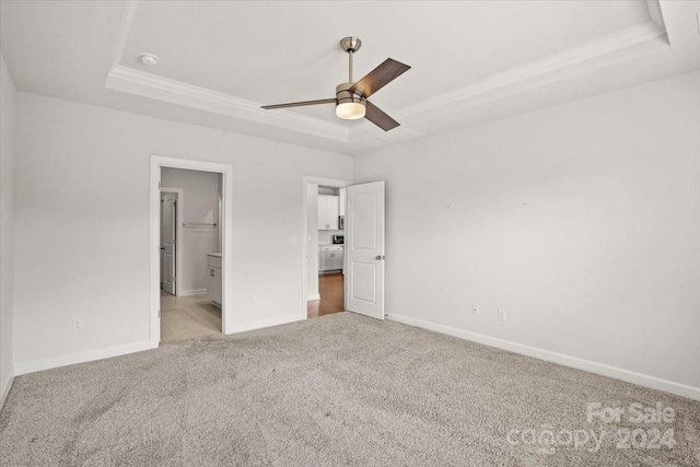 unfurnished bedroom with light colored carpet, ceiling fan, a raised ceiling, and a walk in closet