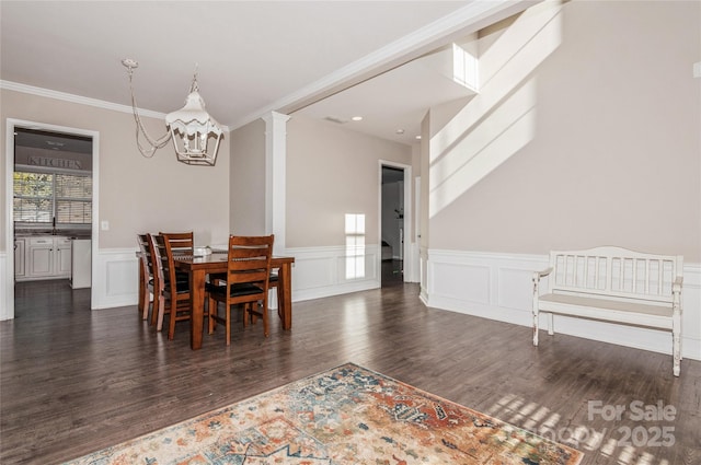 dining room with dark wood-type flooring, ornate columns, crown molding, and a notable chandelier