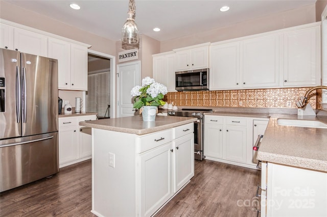 kitchen with stainless steel appliances, a kitchen island, pendant lighting, white cabinets, and sink