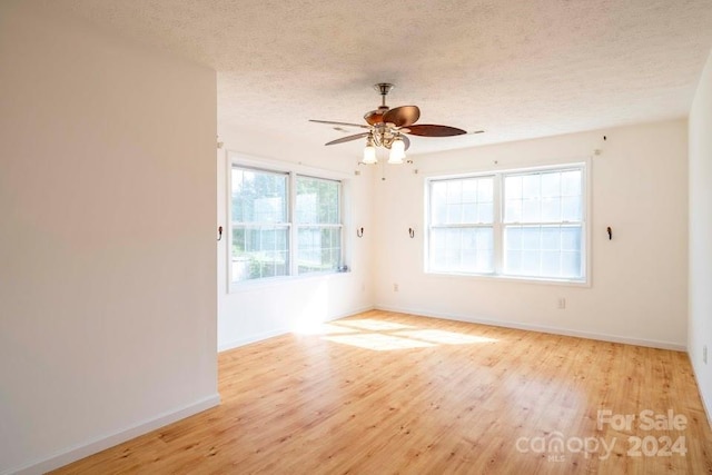 empty room with ceiling fan, light hardwood / wood-style floors, a healthy amount of sunlight, and a textured ceiling