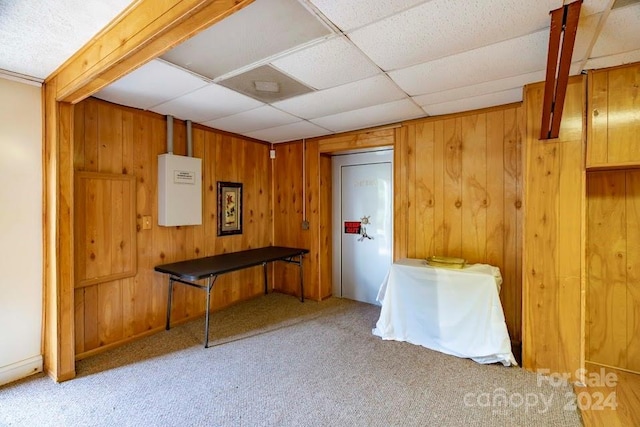 interior space with light carpet, a drop ceiling, and wood walls