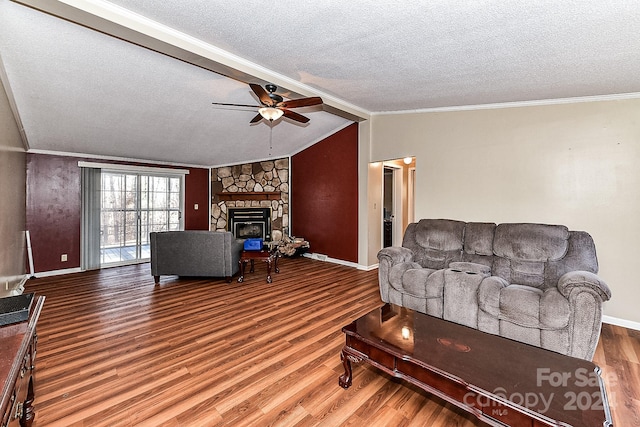 living room with ceiling fan, a stone fireplace, lofted ceiling with beams, wood-type flooring, and a textured ceiling