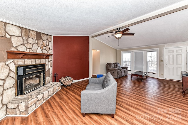 living room with a textured ceiling, ceiling fan, wood-type flooring, lofted ceiling with beams, and a stone fireplace