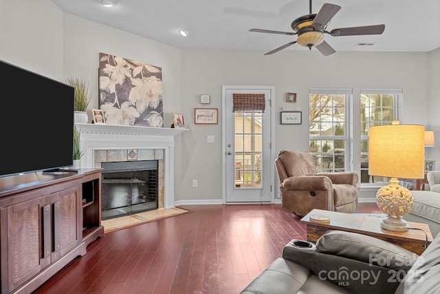 living room with dark hardwood / wood-style flooring, ceiling fan, and a tiled fireplace