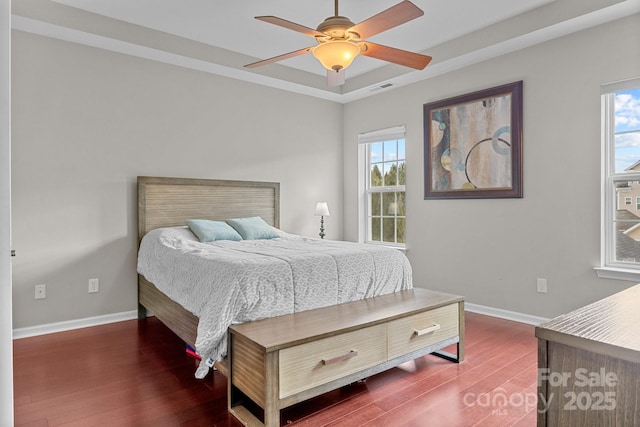 bedroom featuring ceiling fan, dark hardwood / wood-style flooring, a tray ceiling, and multiple windows