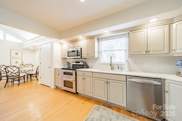 kitchen with decorative backsplash, stainless steel appliances, sink, beamed ceiling, and light hardwood / wood-style floors