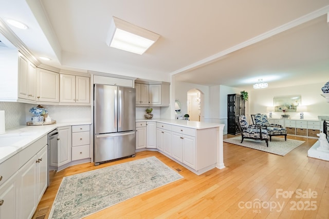 kitchen featuring kitchen peninsula, light stone countertops, light wood-type flooring, backsplash, and stainless steel appliances