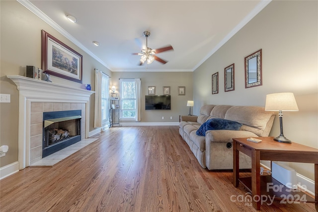 living room with a tiled fireplace, crown molding, light hardwood / wood-style flooring, and ceiling fan