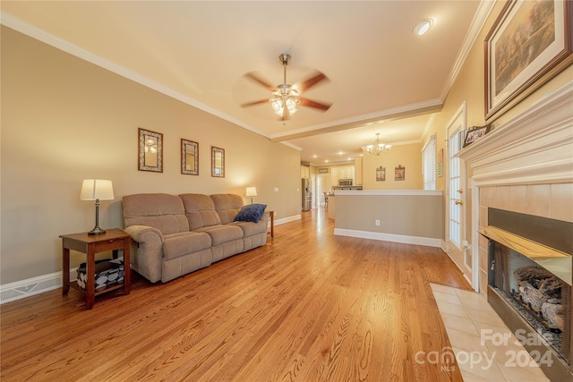 living room featuring crown molding, a fireplace, ceiling fan with notable chandelier, and light hardwood / wood-style flooring