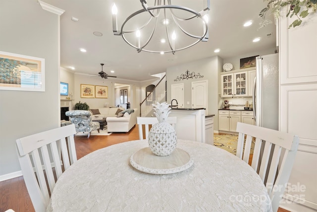 dining space featuring ornamental molding, ceiling fan with notable chandelier, and dark wood-type flooring