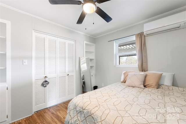 bedroom with a wall mounted air conditioner, ornamental molding, ceiling fan, wood-type flooring, and a closet