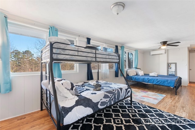 bedroom with hardwood / wood-style flooring, a wall mounted AC, and ceiling fan