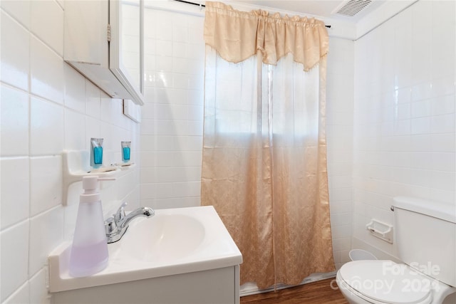 bathroom featuring wood-type flooring, vanity, toilet, and tile walls