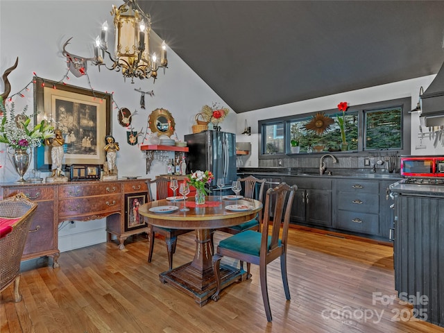 dining room with a notable chandelier, light wood-type flooring, sink, and vaulted ceiling