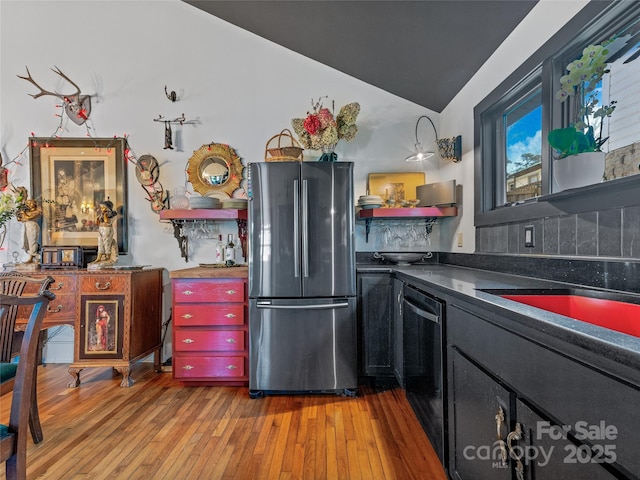 kitchen featuring appliances with stainless steel finishes, light hardwood / wood-style floors, vaulted ceiling, and tasteful backsplash