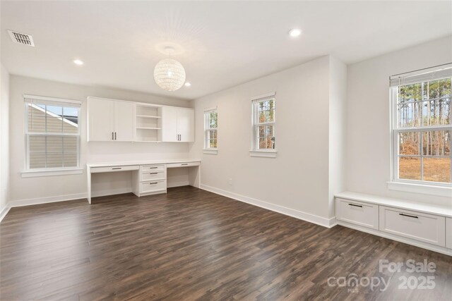 unfurnished office featuring a wealth of natural light, built in desk, and dark wood-type flooring