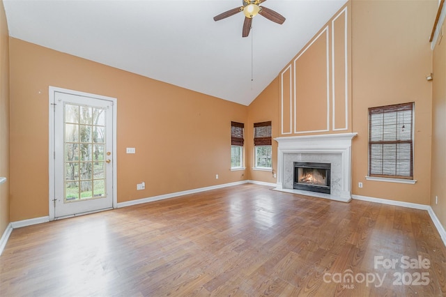 unfurnished living room with high vaulted ceiling, a high end fireplace, light wood finished floors, baseboards, and ceiling fan