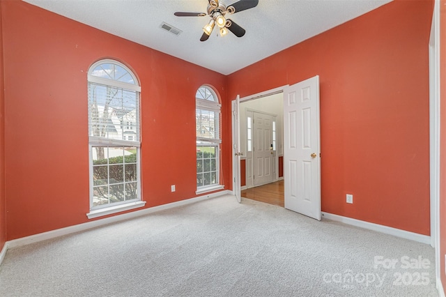 carpeted spare room featuring visible vents, a textured ceiling, baseboards, and a ceiling fan