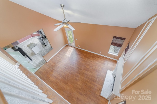 unfurnished living room with vaulted ceiling, baseboards, a ceiling fan, and wood finished floors