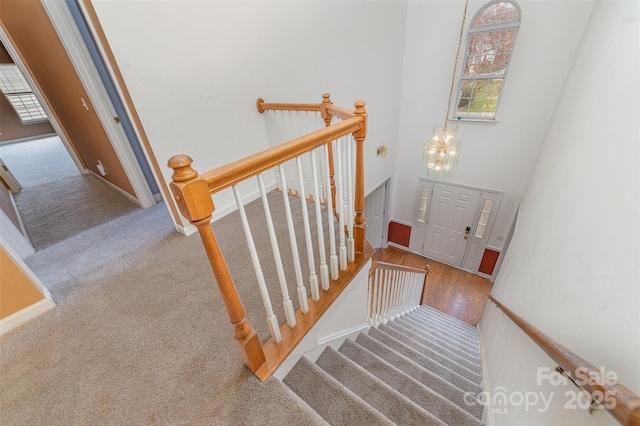 staircase featuring wood finished floors, baseboards, a notable chandelier, a towering ceiling, and carpet flooring