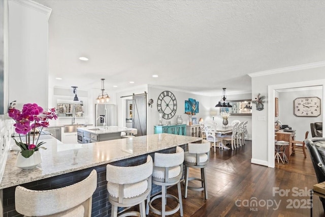 kitchen with a barn door, ornamental molding, decorative light fixtures, kitchen peninsula, and a breakfast bar area