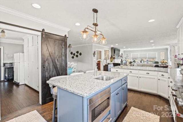 kitchen featuring a kitchen island with sink, sink, a barn door, white cabinetry, and stainless steel appliances