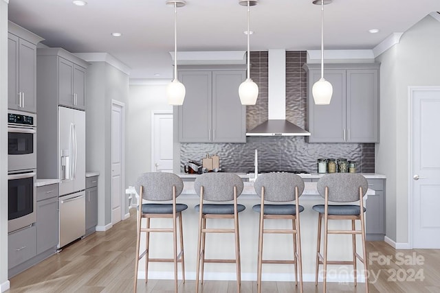 kitchen with refrigerator with ice dispenser, decorative light fixtures, a kitchen island with sink, and wall chimney range hood