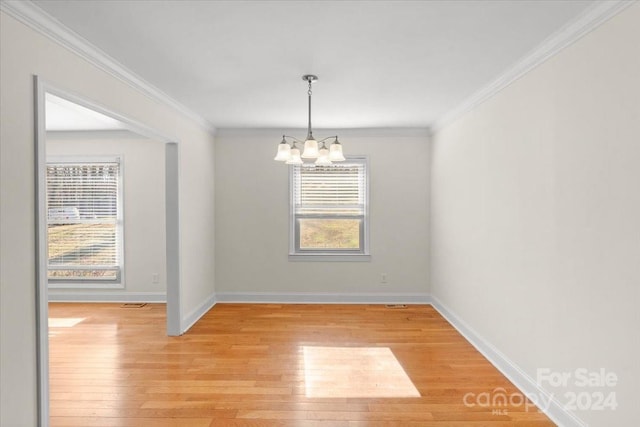 empty room featuring light wood-type flooring, crown molding, and a chandelier