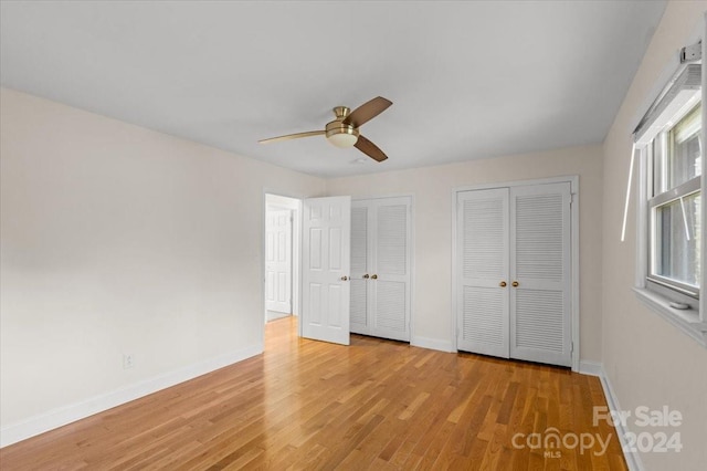 unfurnished bedroom featuring light wood-type flooring, ceiling fan, and multiple closets