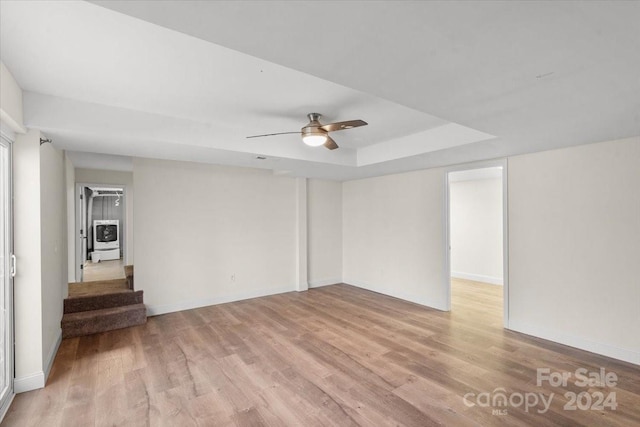 empty room featuring ceiling fan, a tray ceiling, and light hardwood / wood-style flooring