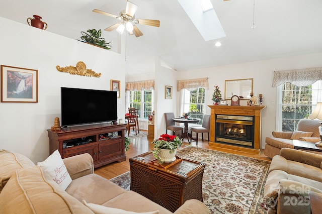 living room with light wood-type flooring, lofted ceiling with skylight, ceiling fan, and plenty of natural light