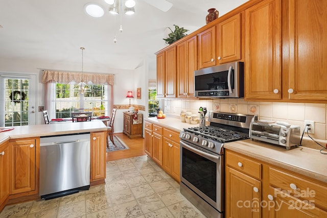 kitchen with decorative backsplash, stainless steel appliances, vaulted ceiling, a chandelier, and hanging light fixtures