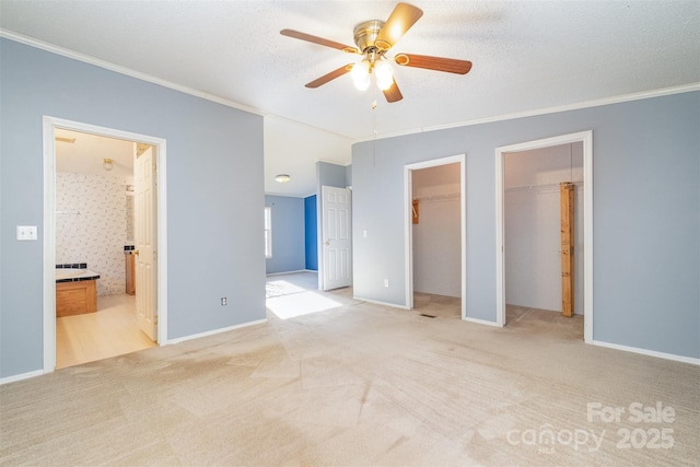 unfurnished bedroom featuring light carpet, ceiling fan, a spacious closet, ornamental molding, and connected bathroom