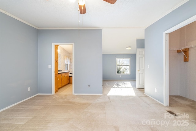 unfurnished bedroom featuring ceiling fan, crown molding, a spacious closet, connected bathroom, and a closet