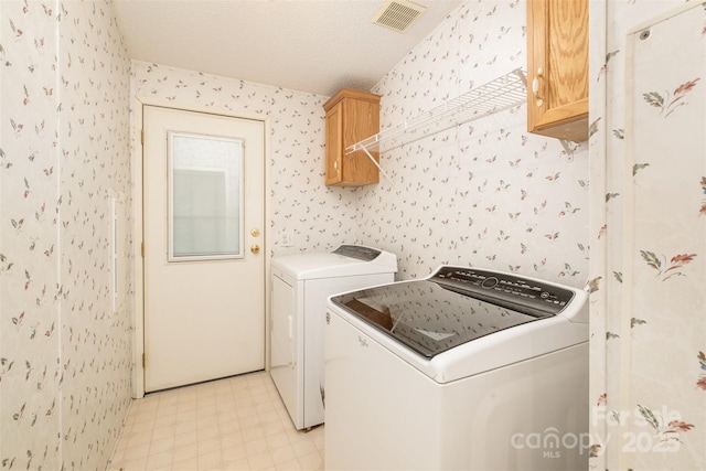 laundry room featuring cabinets, a textured ceiling, and washing machine and clothes dryer