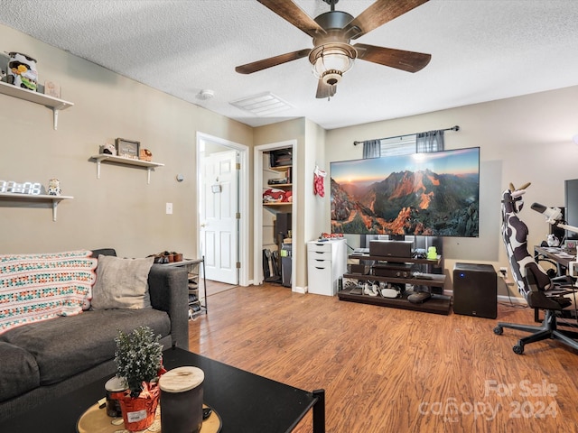 living room with a textured ceiling, light wood-type flooring, and ceiling fan