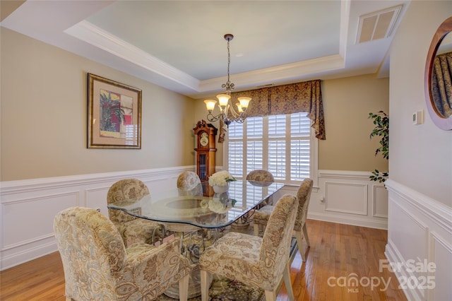 dining room with a chandelier, a raised ceiling, ornamental molding, and light hardwood / wood-style flooring