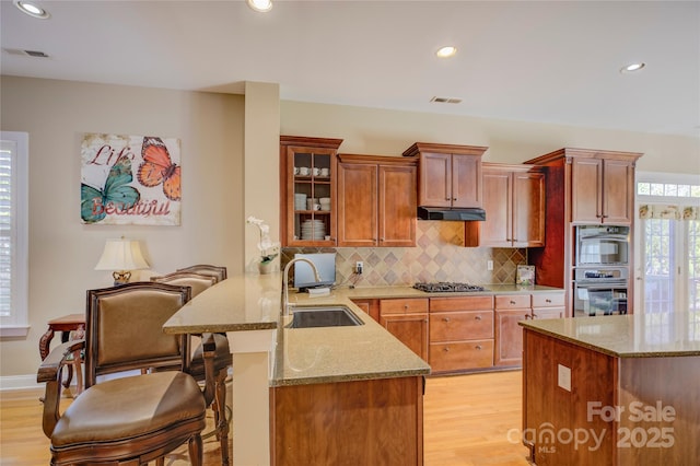 kitchen featuring kitchen peninsula, decorative backsplash, appliances with stainless steel finishes, a kitchen breakfast bar, and sink